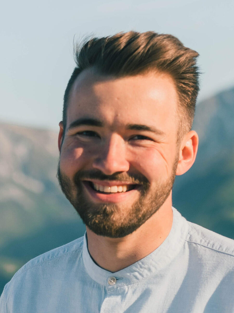 Man gently smiles at the camera with soft blue mountains behind him - Photographed by philipp wuthrich